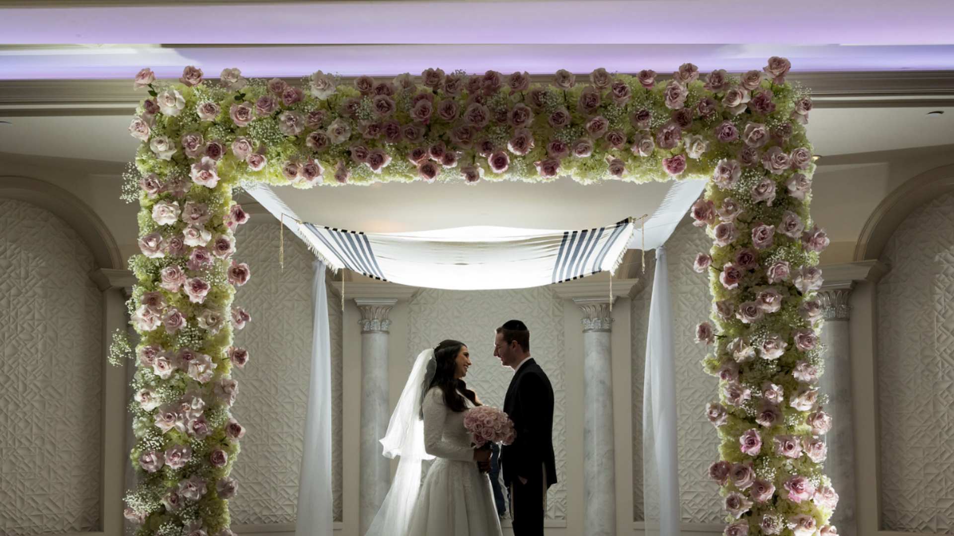 Jewish couple under a floral chuppah canopy at a kosher wedding ceremony